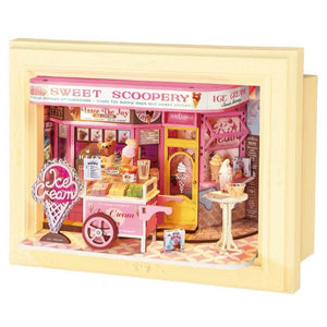 مجسم متجر آيس كريم وردي داخل إطار أصفر، مع عربة تقديم وطاولة صغيرة